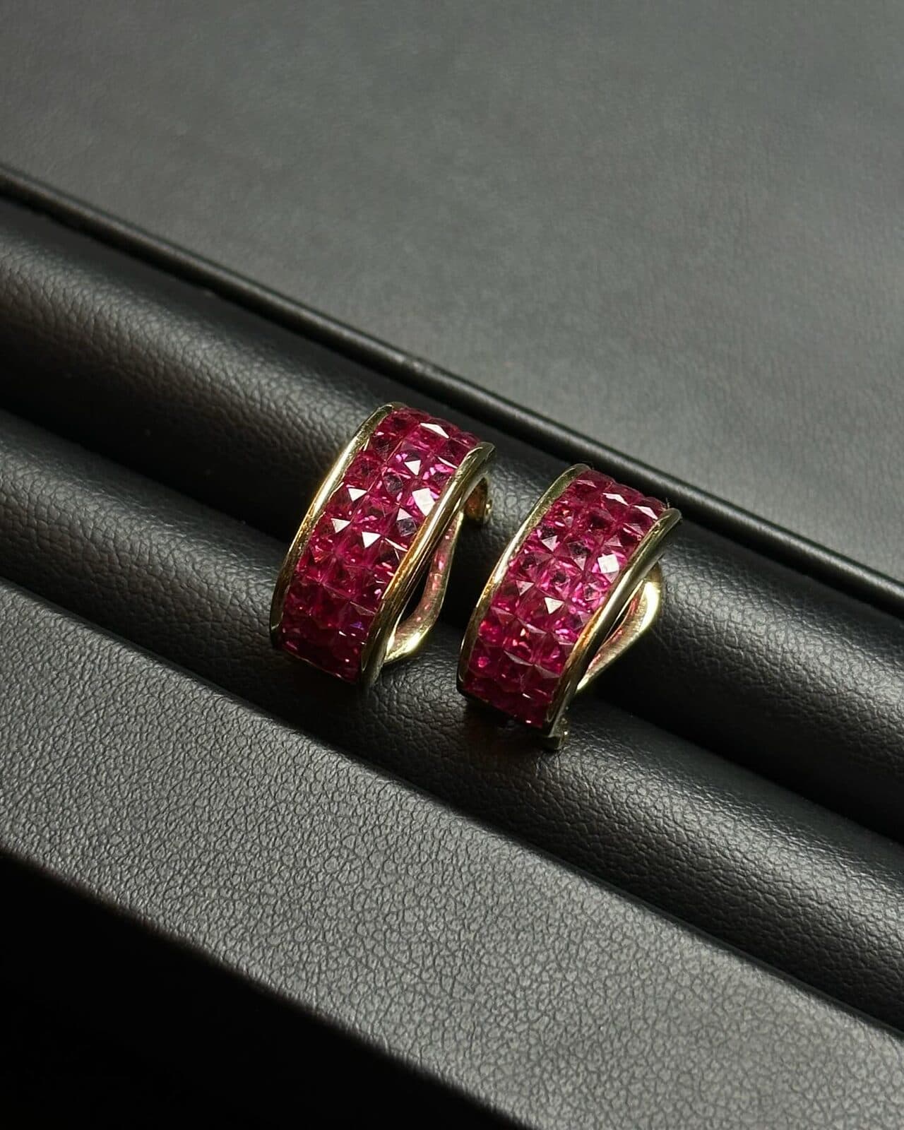 A pair of earrings set with red stones on black leather.