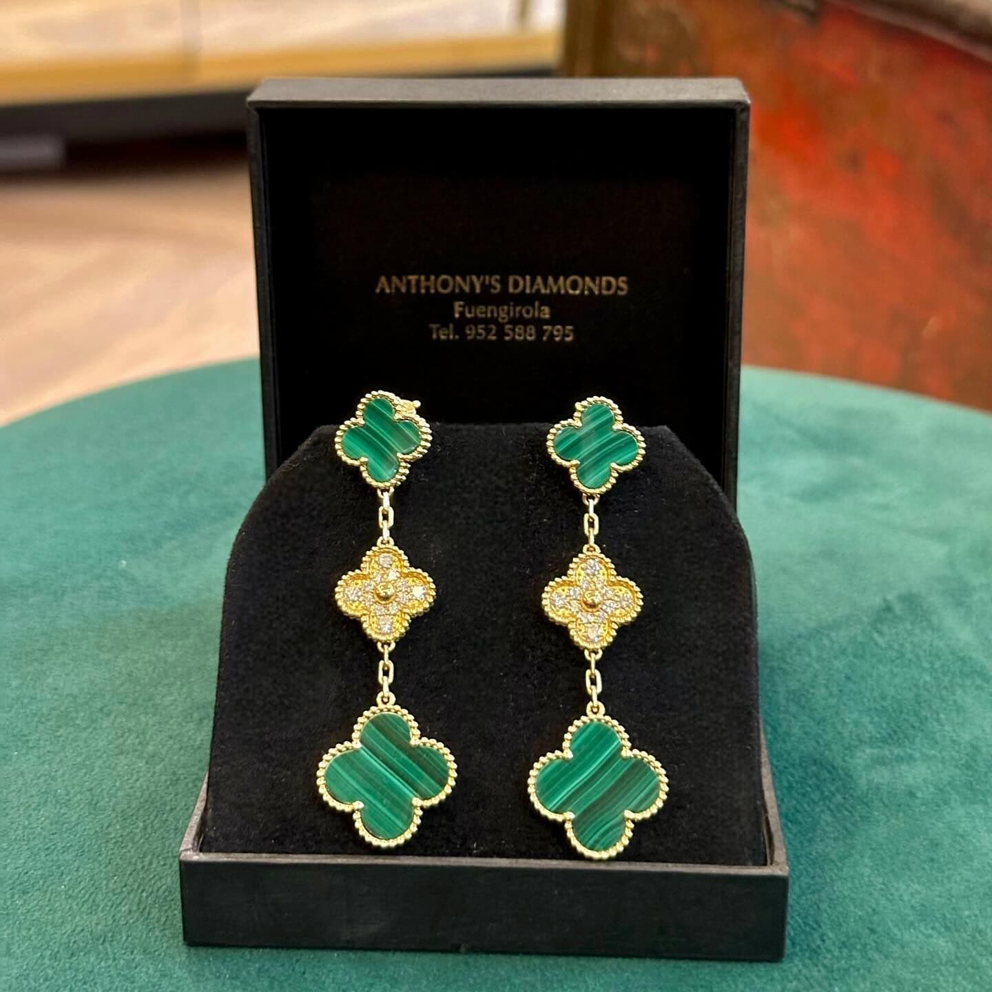 A pair of green and gold-coloured drop earrings in an Anthony's Diamonds box.