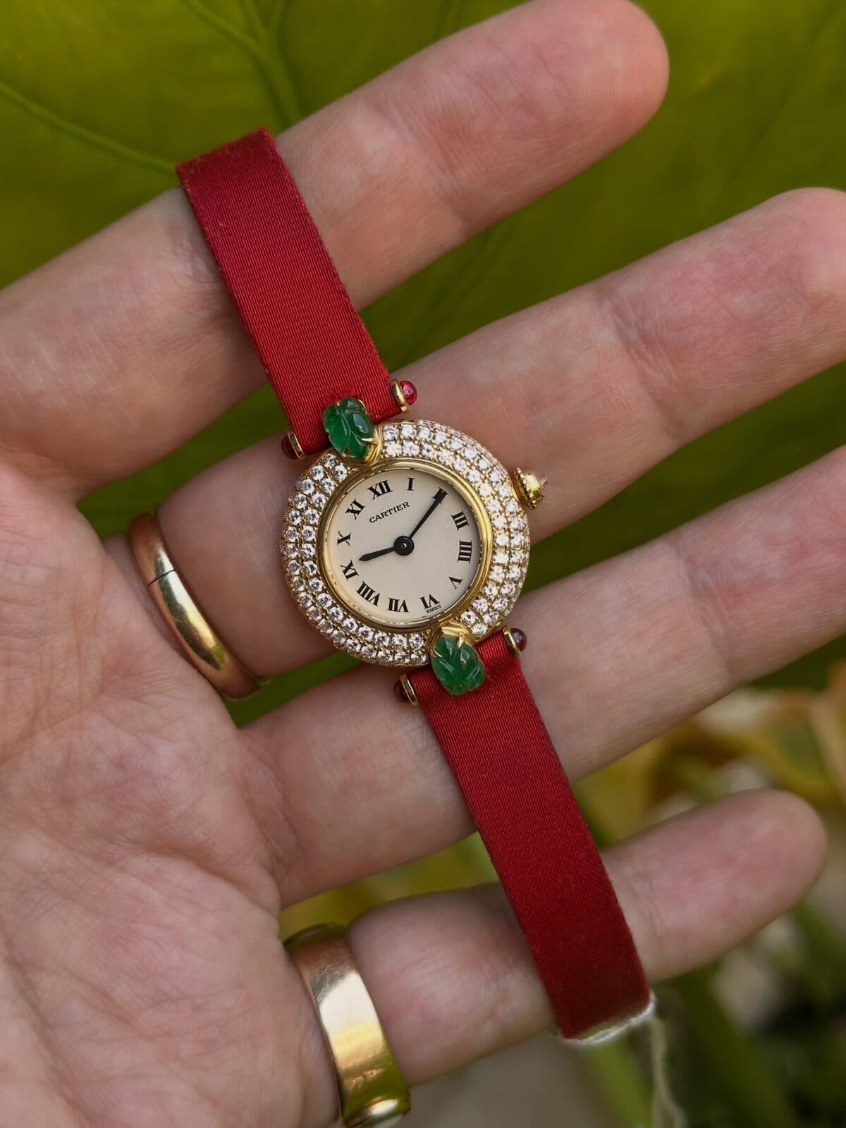 A small watch on a red strap in an open palm.