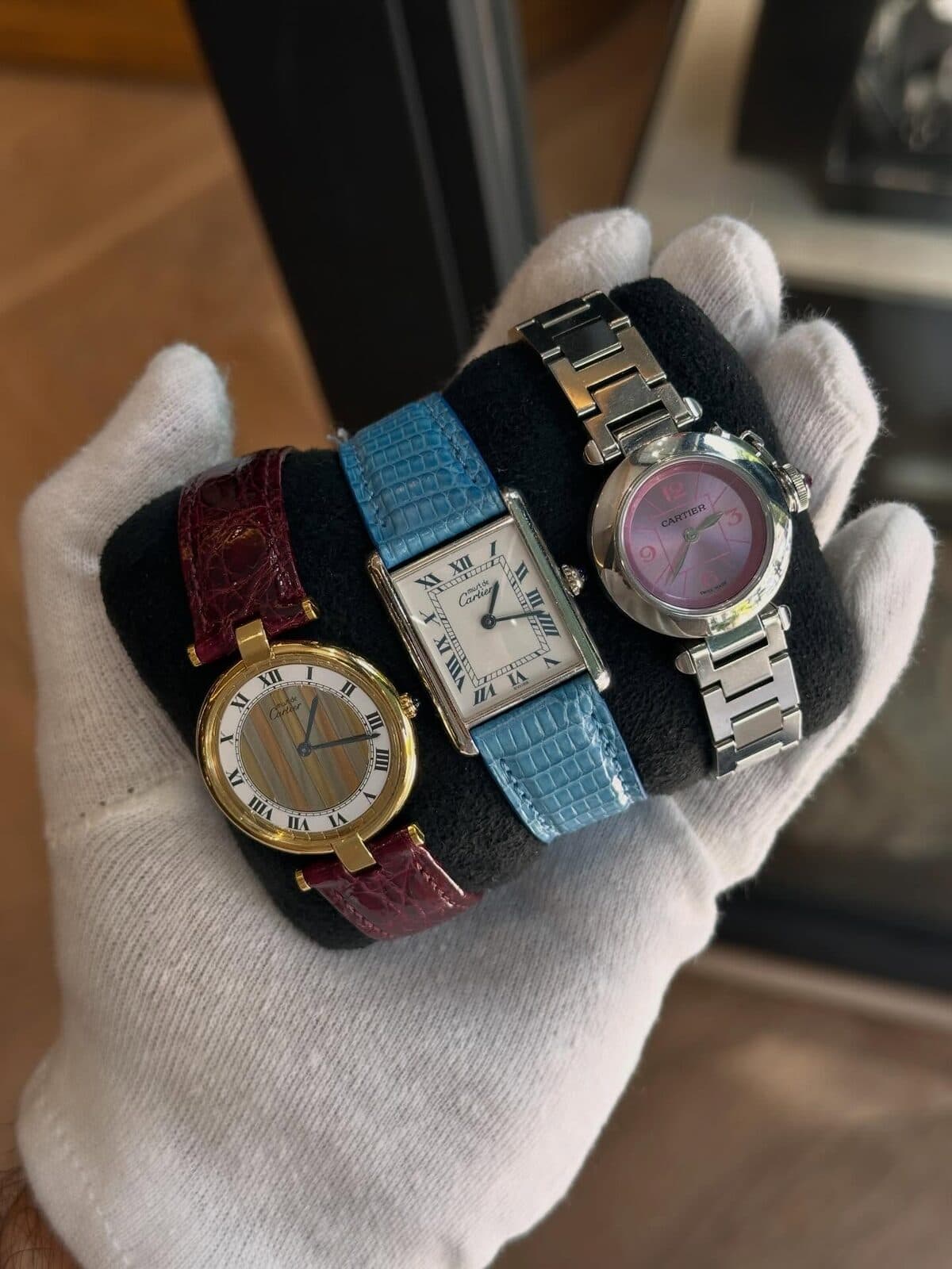 A gloved hand holding three watches on a cushion.
