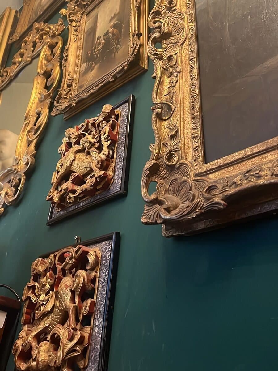 Gilt-framed paintings and carved panels on a dark green wall.