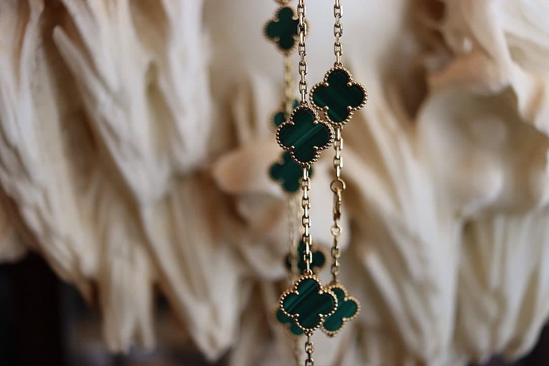 A long necklace of green clover motifs hanging against cream.